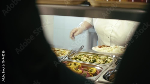 Chef standing behind full lunch service station with assortment of food in trays.