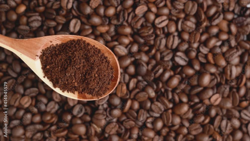 Dark wood spoon with ground coffee inside. Rotating coffee beans in the background