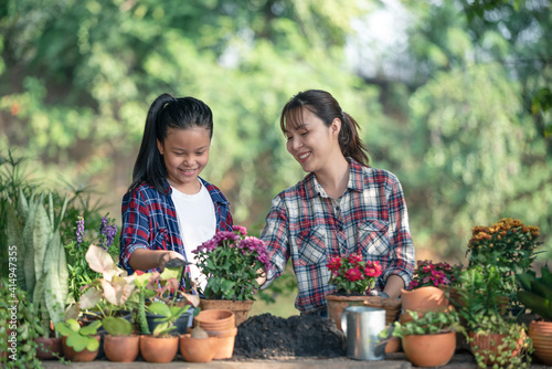 Lovely teenage girl helps her mother pant the flower. Mom and her daughter engaged in gardening near window at home in weekend. Family having a happy time doing thing together.