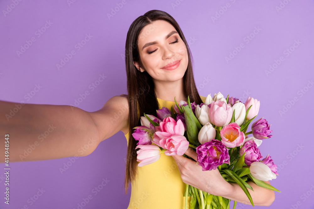 Self-portrait of attractive cheerful dreamy girl holding hugging tulips enjoying good mood isolated over violet purple pastel color background