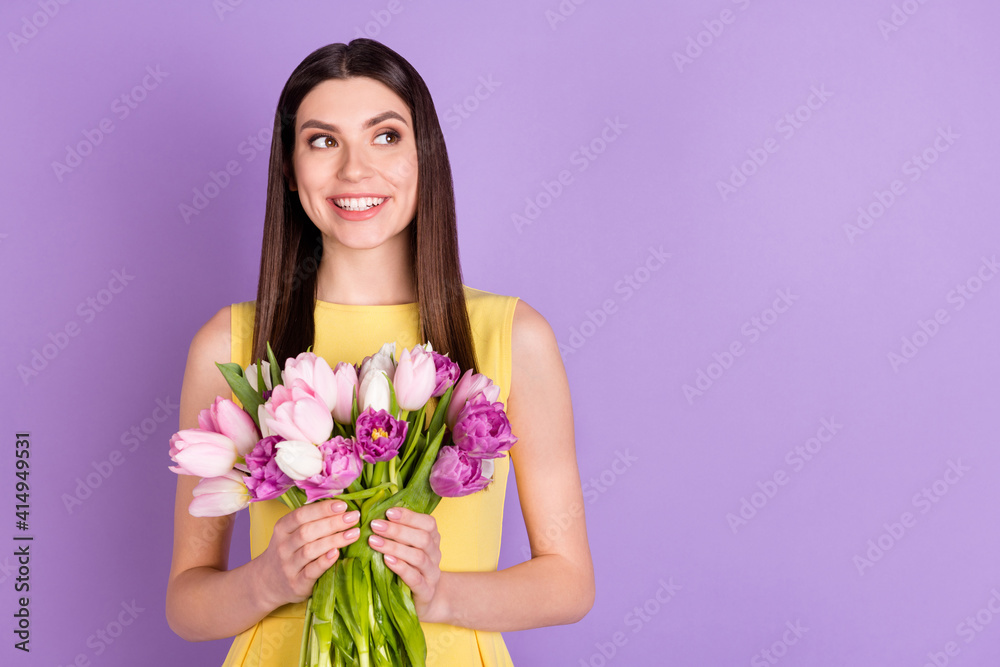 Portrait of attractive cheerful girl holding in hands tulips looking aside copy space isolated over violet purple pastel color background