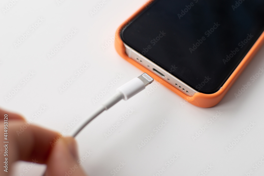 Close-up smartphone with lightning Cable on white Background in orange case. Quick charge phone. Close-up smartphone with lightning Cable on white Background in orange case. Quick charge phone.