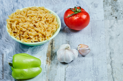 A bowl of raw pasta with tomato, pepper, and garlic on blue background