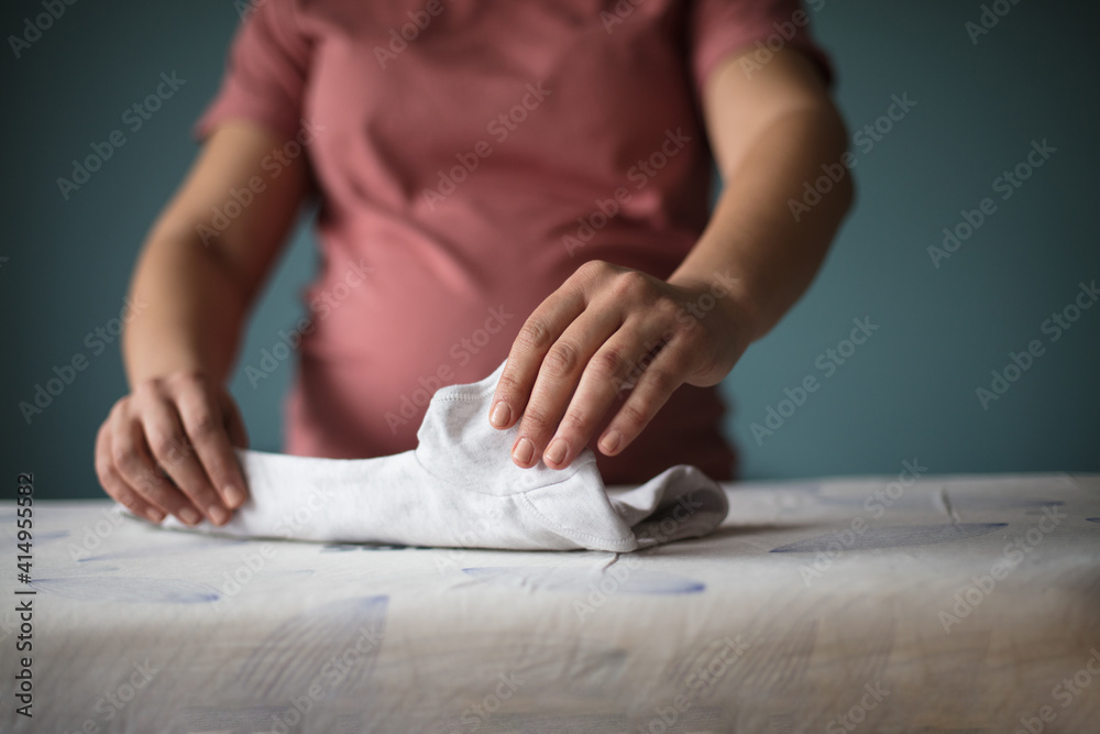 Pregnant woman at home preparing baby laundry.