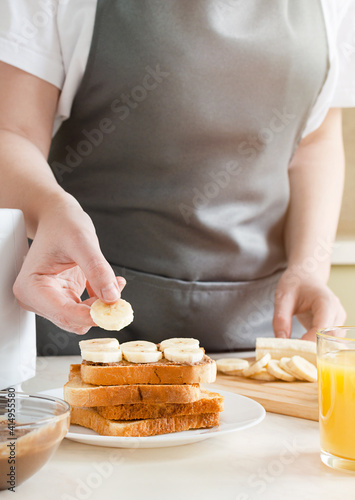 woman cooking sweet toast with peanut butter and banana. European breakfast with toast and juice