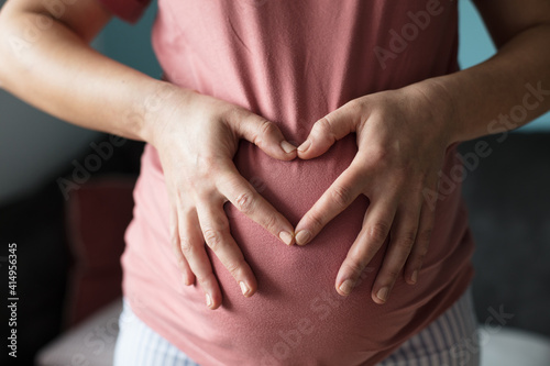  Pregnant woman holding her belly and making a heart shape.