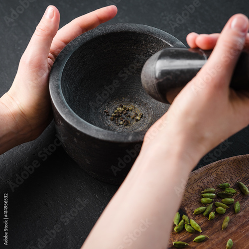 A woman pounding cardamom in a stone mortar on a dark background