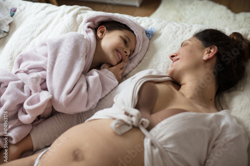 Pregnant woman with her daughter lying together on bed.