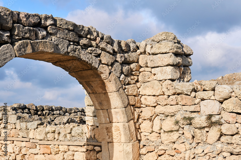 fragment of a destroyed antique house walls with arch against the sky