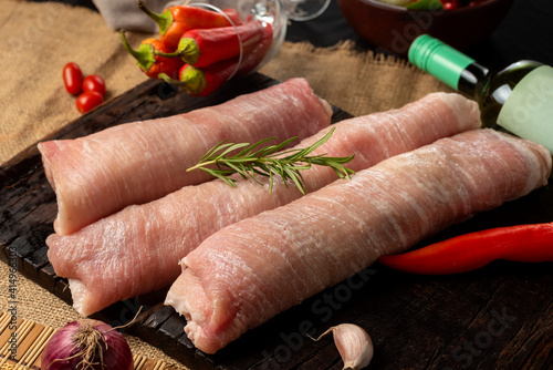 raw rolled pork meat presented on a wooden board with rosemary, onion, red peppers and garlic with pepper. photo