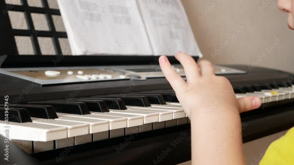 A little boy learns to play synthesizer pushing the white keys one by one close-up