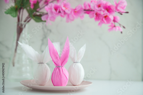 Three eggs bunny in a colored paper wrapper on a plate and table in a cherry blossoms. The Easter holiday