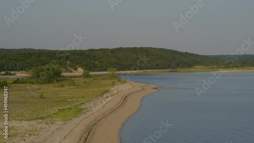 Forward Aerial Pan of a Sandy Beach Shore Near Dense Forest Trees photo