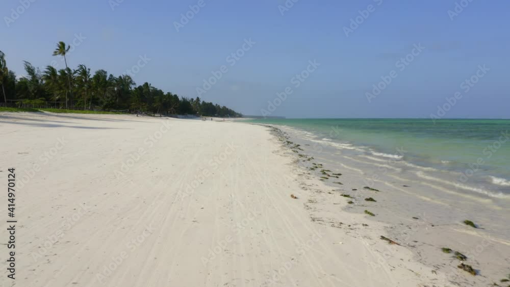 Aerial drone tracking shot flying fast along a perfect palm tree fringed sandy beach paradise, with waves lapping at Paje Beach, Zanzibar, Tanzania