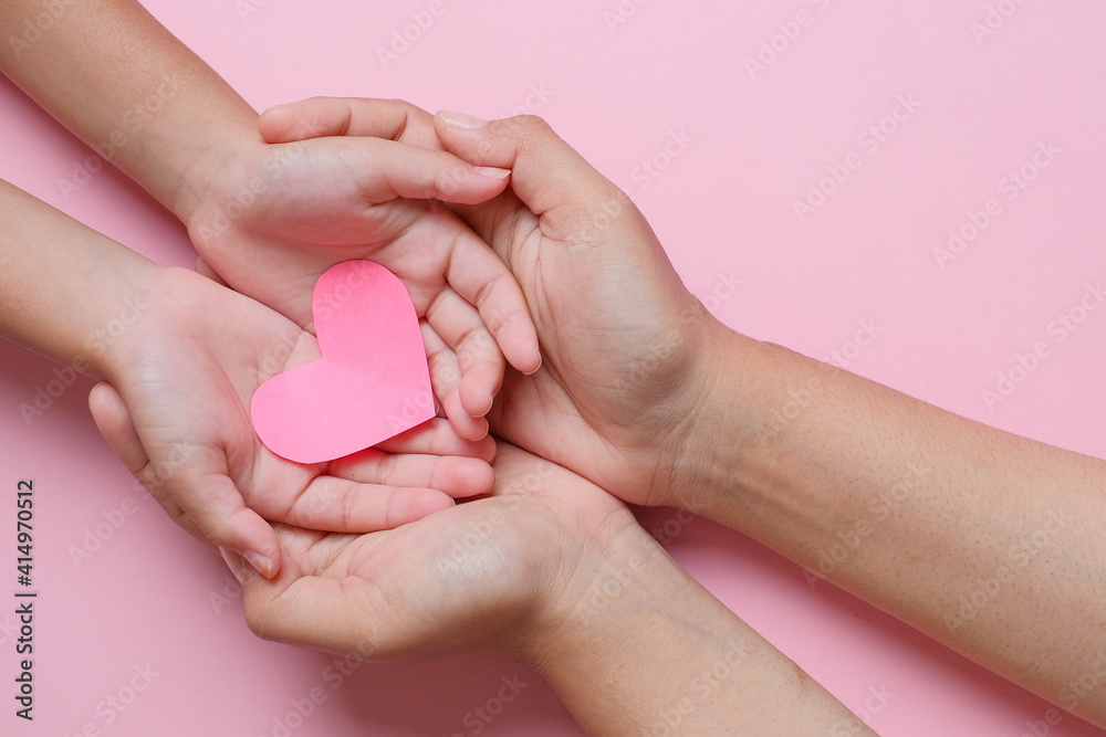 Adult and child hands holding red heart over pink background. Love, healthcare, family, insurance, donation concept Adult and child hands holding red heart over pink background. Love, healthcare, family, insurance, donation concept