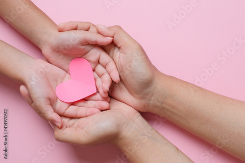 Adult and child hands holding red heart over pink background. Love, healthcare, family, insurance, donation concept