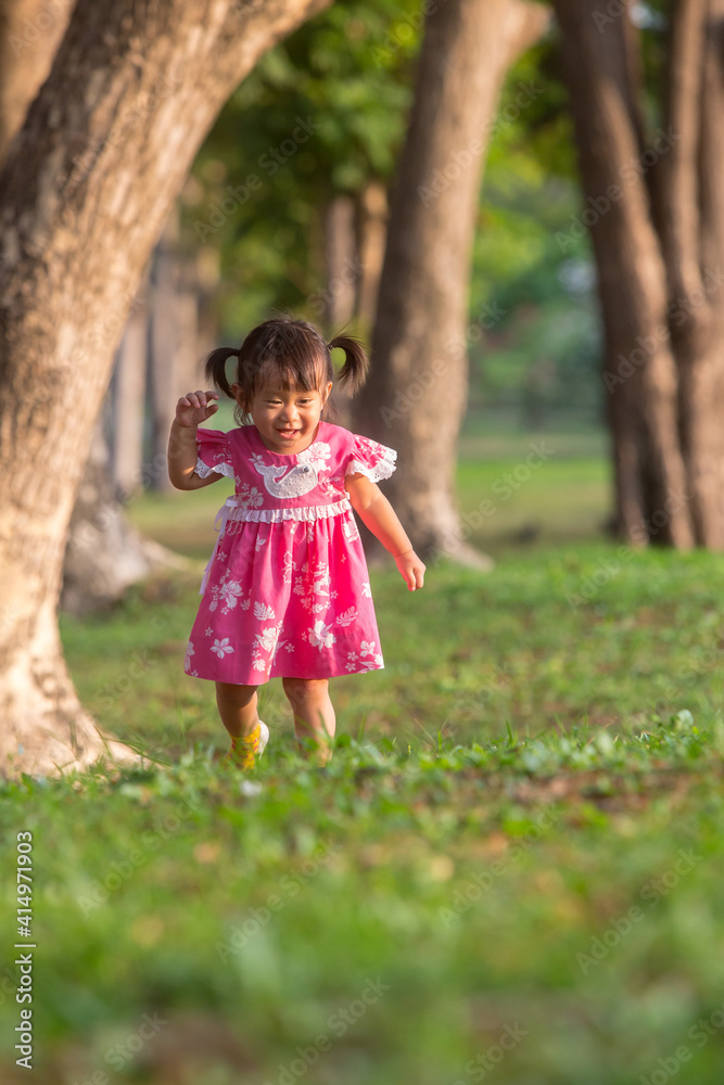A Lovely asian little girl wear a pink dress is standing in the park at the evening sunshine A Lovely asian little girl wear a pink dress is standing in the park at the evening sunshine