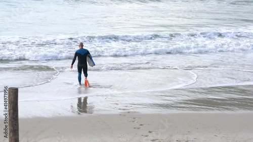 Hombre en la playa andando por la arena, entrando al agua, con aletas y bodyboard para practicar deporte. photo