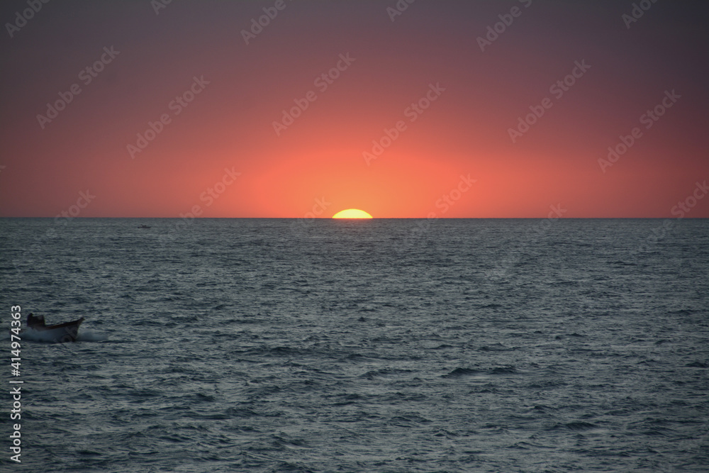 Red sunset on the sea with the small boat of a fisherman reintraing towards the coast.