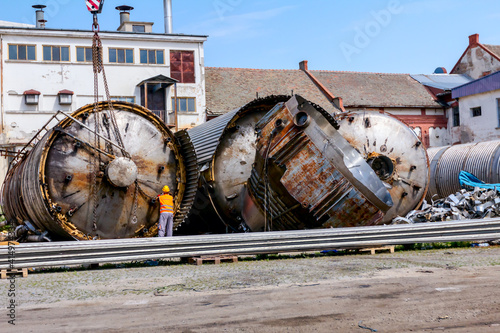 Mobile crane lay down big old metal tank Worker is helping to keep balance and direction