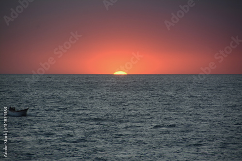 Red sunset on the sea with the small boat of a fisherman reintraing towards the coast.