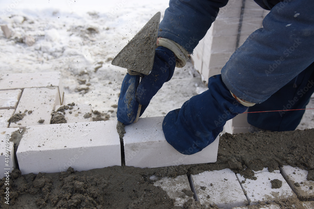 A bricklayer levels cement, makes a concrete wall, builds a residential building, a worker lays bricks, aligns with a spatula. A bricklayer levels cement, makes a concrete wall, builds a residential building, a worker lays bricks, aligns with a spatula.