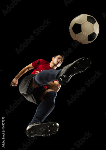 Young caucasian football, soccer player in action, motion isolated on black background, look from the bottom. Concept of sport, movement, energy and dynamic, healthy lifestyle. Training, practicing.