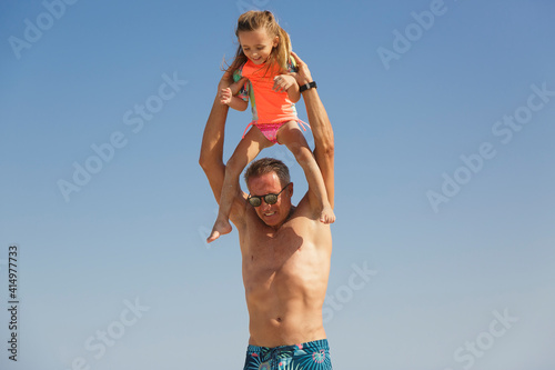 Un padre prende la figlia sulle spalle giocando simpaticamente con lei al mare in spiaggia photo