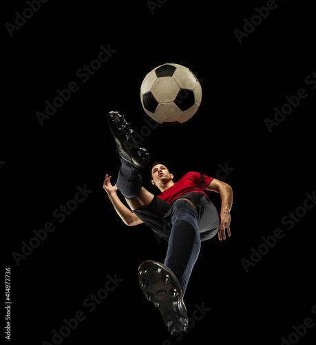 Young caucasian football, soccer player in action, motion isolated on black background, look from the bottom. Concept of sport, movement, energy and dynamic, healthy lifestyle. Training, practicing. © master1305