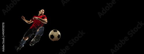 Young caucasian football, soccer player in action, motion isolated on black background, look from the bottom. Concept of sport, movement, energy and dynamic, healthy lifestyle. Flyer with copyspace. © master1305