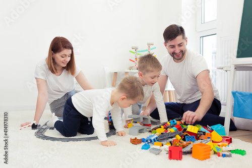 Young family, mom and dad with two young sons, playing with toys in the nursery, happy family having fun together