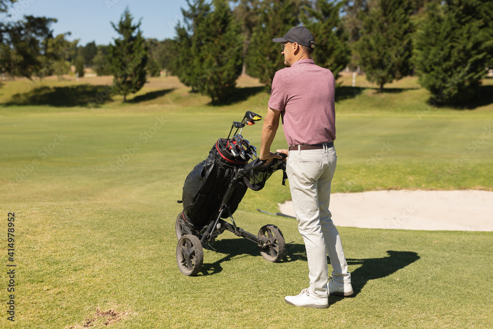 Caucasian senior man walking across golf course holding golf bags Caucasian senior man walking across golf course holding golf bags