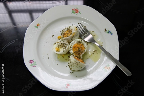 Hard-boiled chicken eggs with oregano, olive oil, black pepper and a fork on a white ceramic plate on a kitchen hob. Top view, selective focus