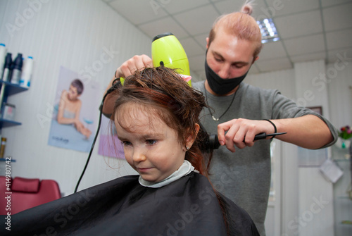 The hairdresser makes a haircut for the child.