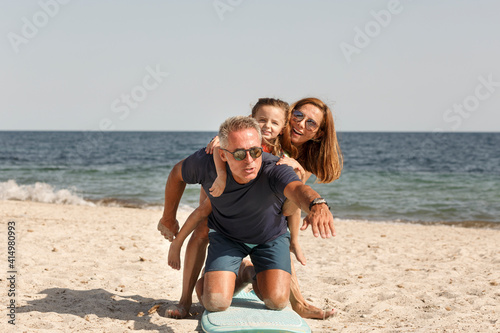 Allegra famiglia composta da padre, madre e figlia si diverte giocando con con una tavola da surf in spiaggia al mare
