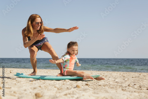 Madre in costume da bagno insegna le basi del surf alla figlia in una spiaggia al mare.