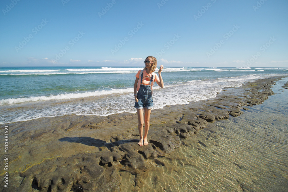 Woman wearing orange t-shirt and shorts at rocky beach looking away. Lifestyle. Woman wearing orange t-shirt and shorts at rocky beach looking away. Lifestyle.