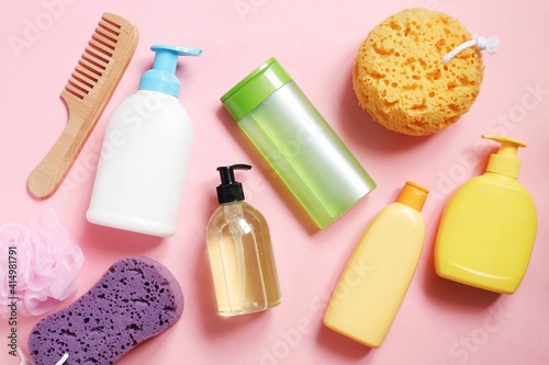 Toiletries and hygiene products. Wooden comb, shampoo, shower gel, hair conditioner, balm and sponges on a pink background. Flat lay beauty photography