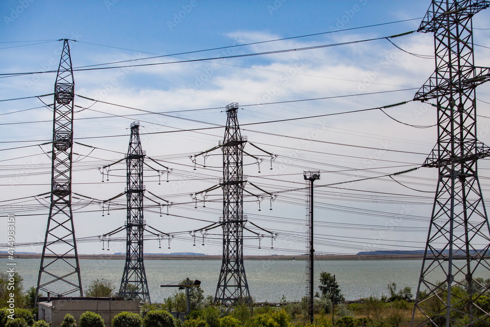 High-voltage transmission line and electric pylons on lake and blue sky with clouds background.