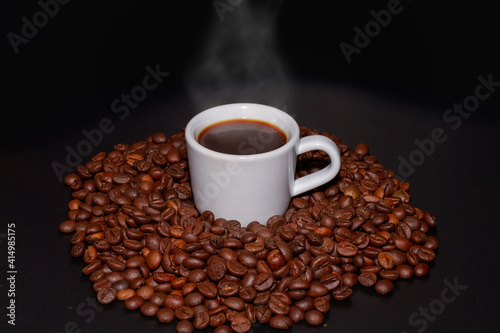 White coffee mug with a coffee drink inside and surrounded by roasted coffee beans of the Robusta variety.
