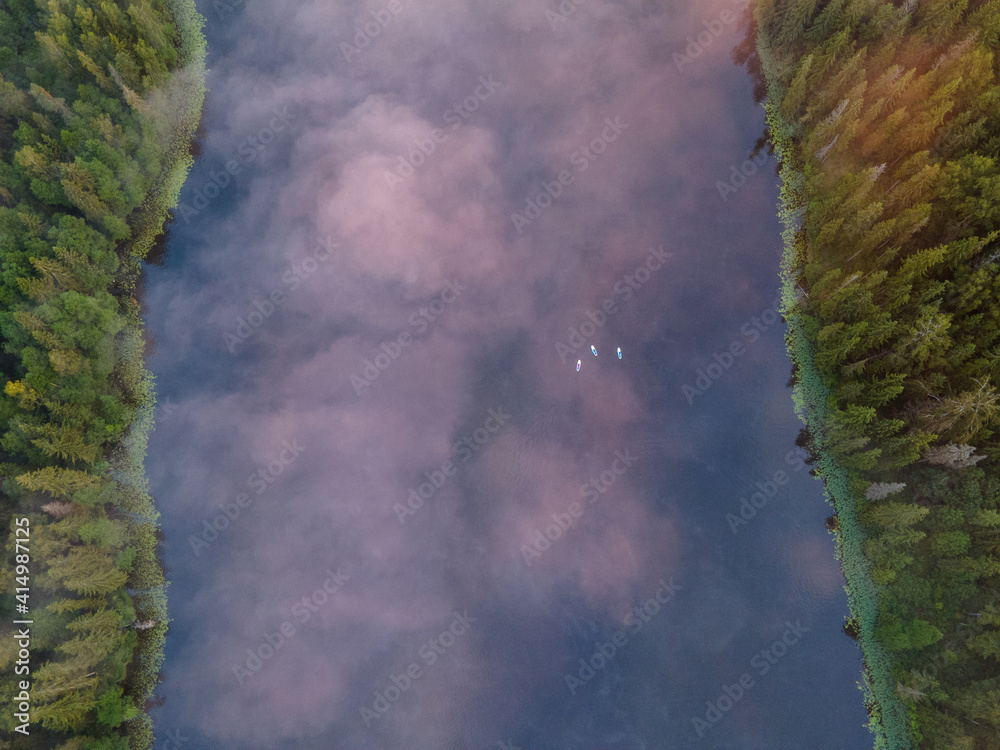 Wonderful view of the lake from the drone early in the morning where people paddle with SUP stand up paddle boards. The fog covers the tops of the trees and the water of the lake