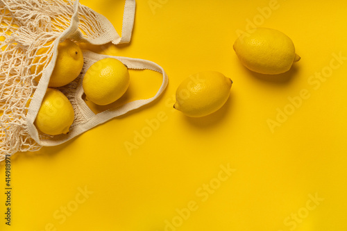 Eco-friendly bag with ripe yellow lemons on yellow background