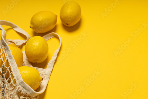 Eco-friendly bag with ripe yellow lemons on yellow background