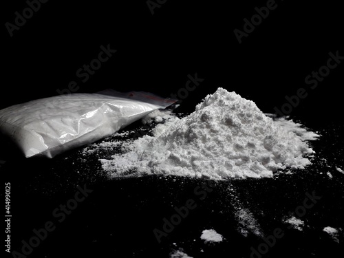 Cocaine drug powder pile and bag on black background