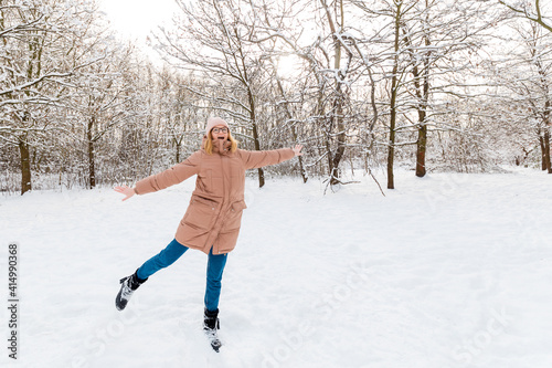Young beautiful happy girl in winter knitted hat posing in winter forest. Snow background