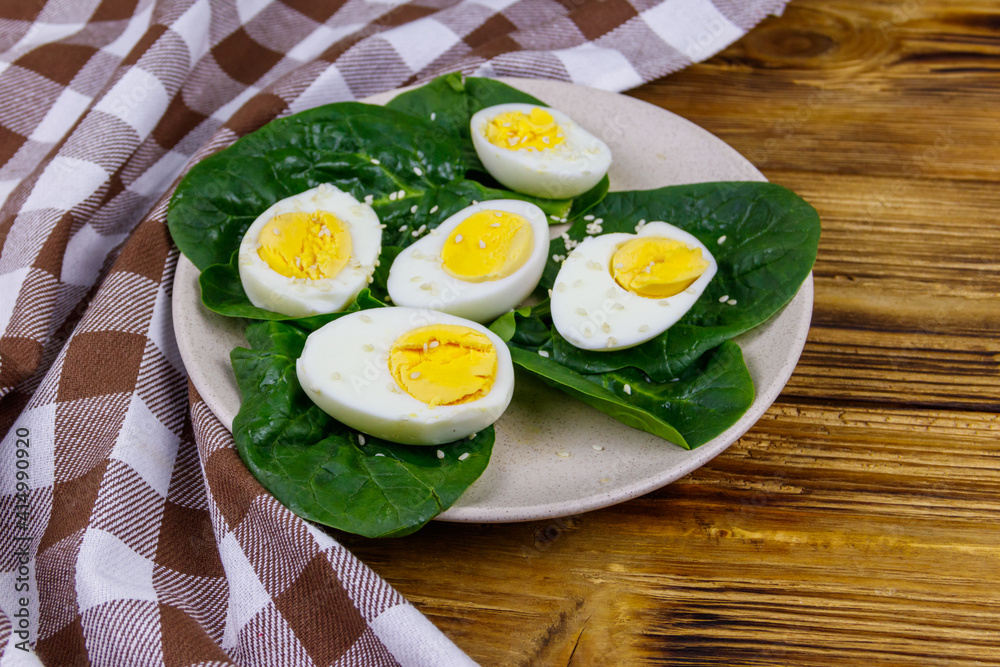 Boiled eggs with fresh spinach leaves and sesame seeds on wooden table Boiled eggs with fresh spinach leaves and sesame seeds on wooden table