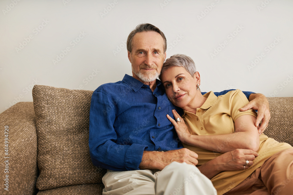 Senior couple embracing on a sofa. Affectionate people hugging at home. Senior couple embracing on a sofa. Affectionate people hugging at home.