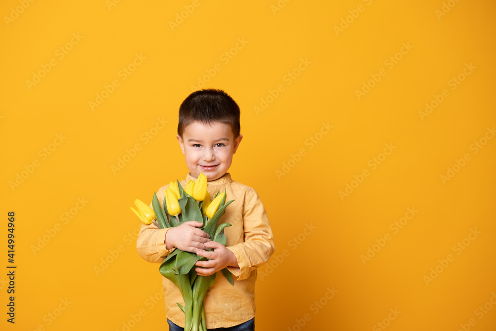 Smiling little boy on yellow studio background. Cheerful happy child with tulips flower bouquet Smiling little boy on yellow studio background. Cheerful happy child with tulips flower bouquet