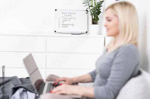 Young adult beautiful woman sitting on bed in bedroom with laptop photo