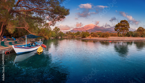 Fototapeta Naklejka Na Ścianę i Meble -  Panoramic sunset view of a mediterranean sea and a motor boat moored at the pier with Mount Tahtali in the background. Paradise vacation and tourism in Tekirova resort in Turkey